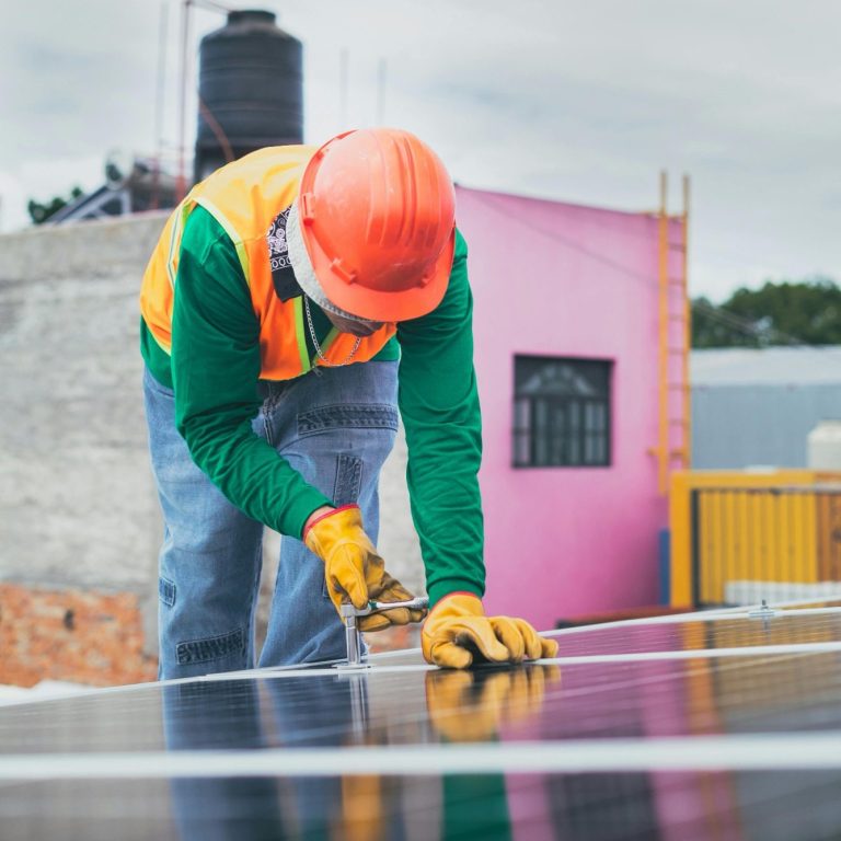 Ein Arbeiter installiert Solarpanele auf einem Gebäude, trägt Helm und Handschuhe.