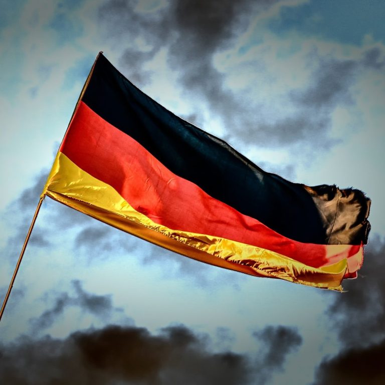 Welle der deutschen Flagge mit Schwarz, Rot und Gold vor wolkigem Himmel.