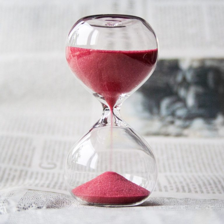 Rote Sanduhr mit fließendem Sand, auf einem Zeitungsblatt platziert.