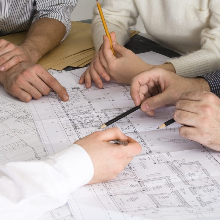 Hände von mehreren Personen, die um einen Architekturplan gruppiert sind.