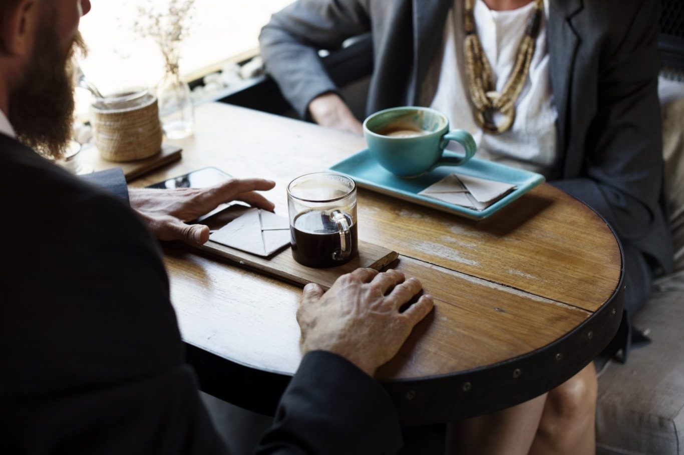 Zwei Personen sitzen an einem Tisch, eine Tasse Kaffee und ein Glas Wasser stehen dort.
